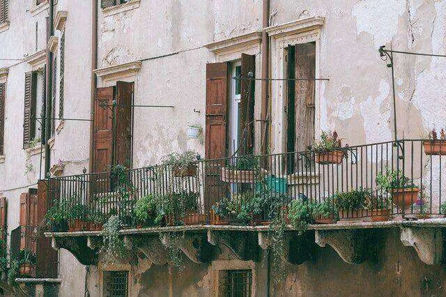 Old building with wooden shutters and balconies with potted plants, showing signs of wear.