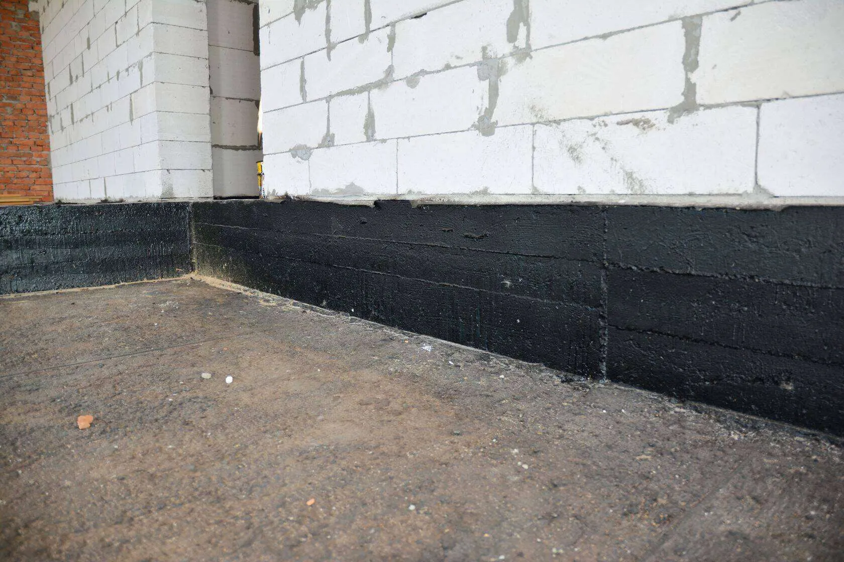 Close-up of a basement wall with black waterproofing membrane applied at the base.