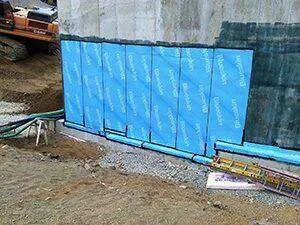 Concrete wall with blue waterproofing membrane panels at a construction site.