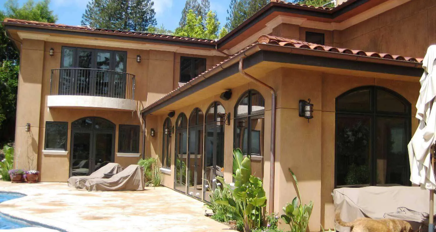 Two-story home with cementitious finish, arched windows, and a balcony, viewed from a poolside patio. — Kentfield area