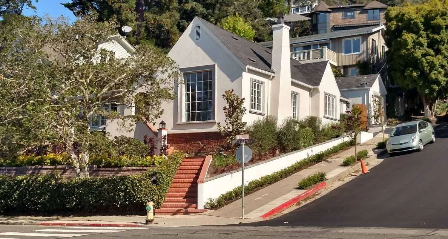White stucco house with brick stairs and landscaping on a sloped street in San Rafael. — Novato area