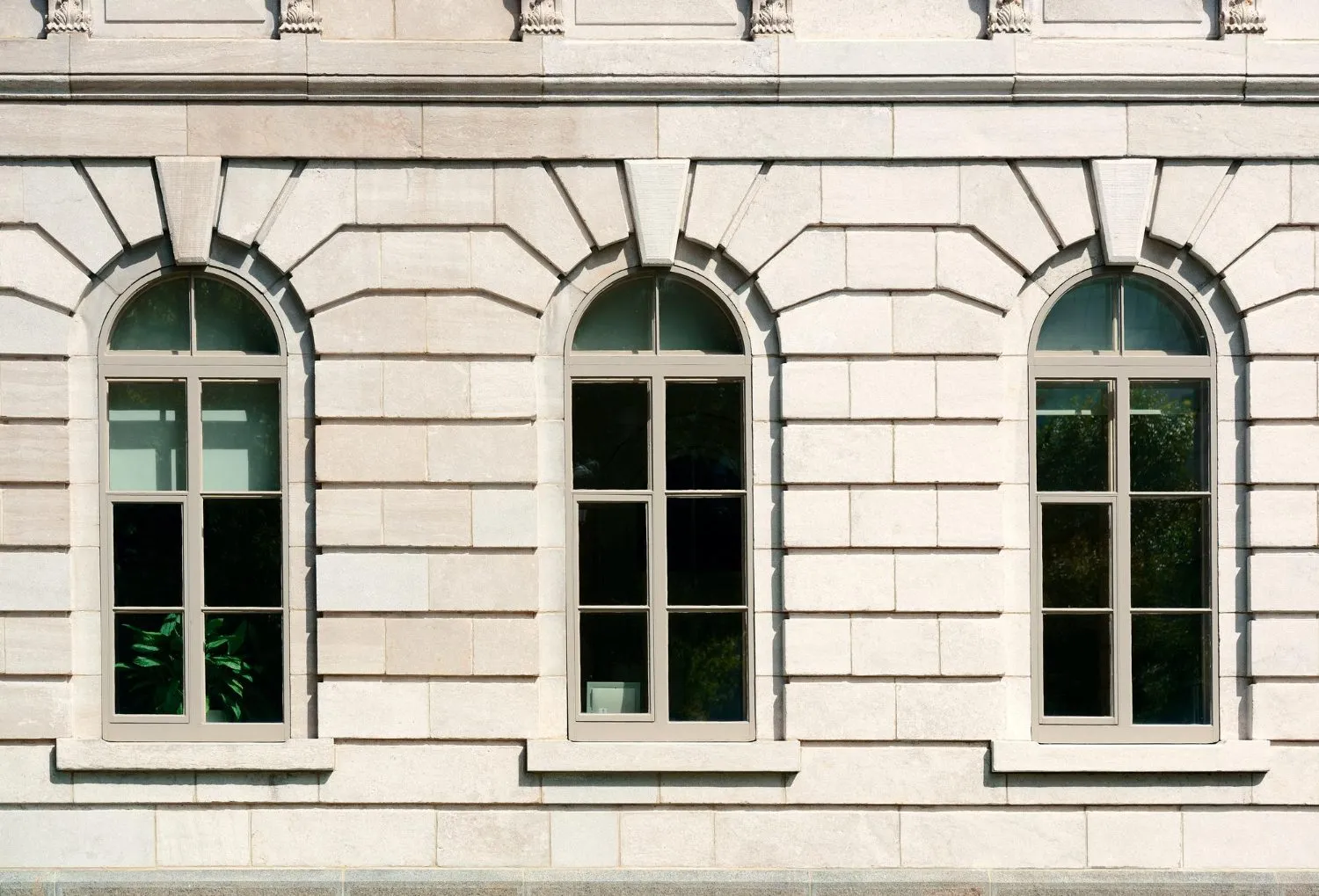 Three arched windows with multiple panes set in a detailed stone facade.