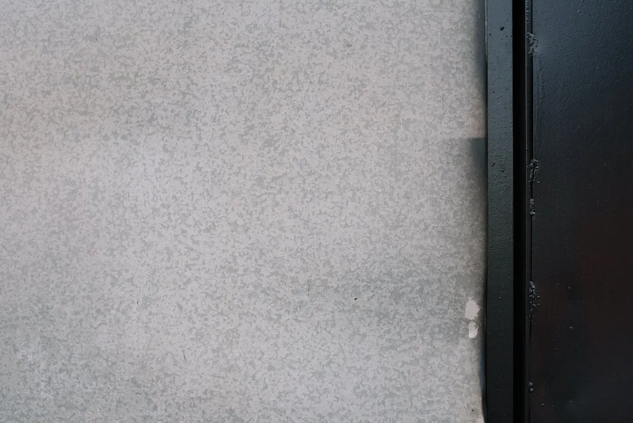 Close-up of a textured stucco wall next to a black metal frame, showing surface detail. — Alameda area