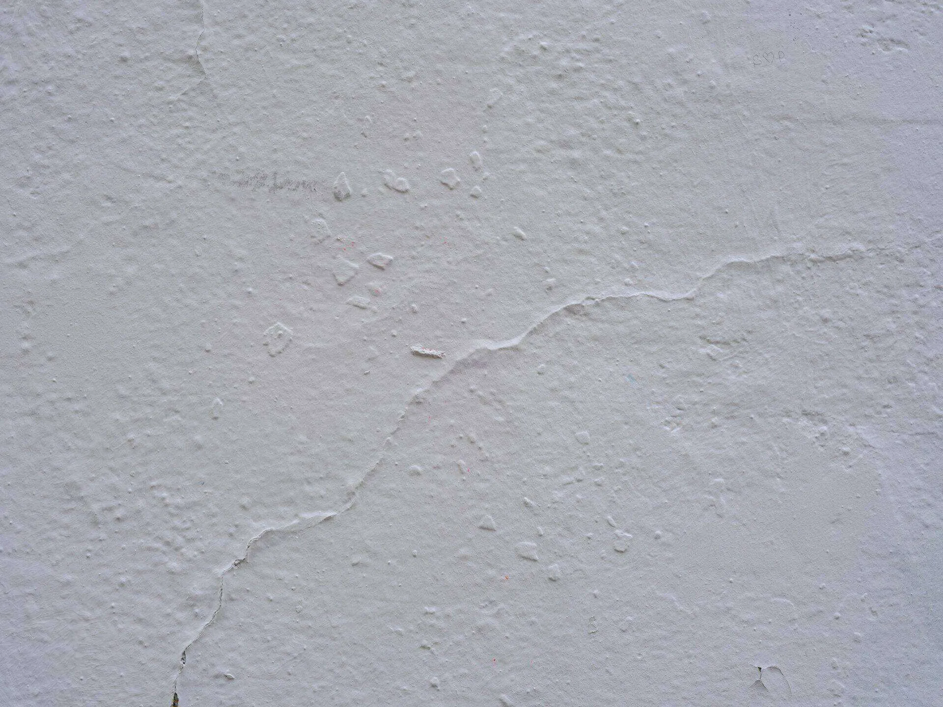 Close-up of a white plaster wall showing texture and visible cracks.