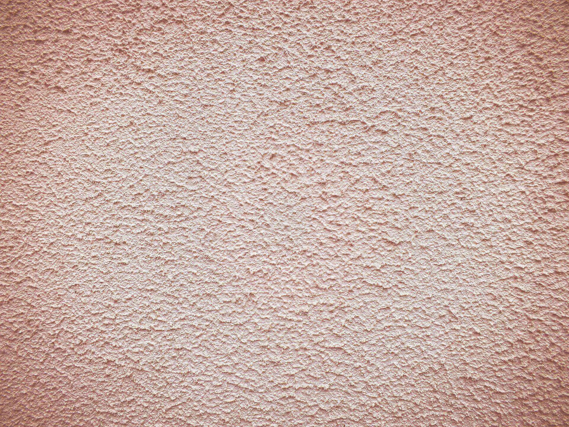 Close-up view of a textured stucco wall with a rough finish in light pink color.