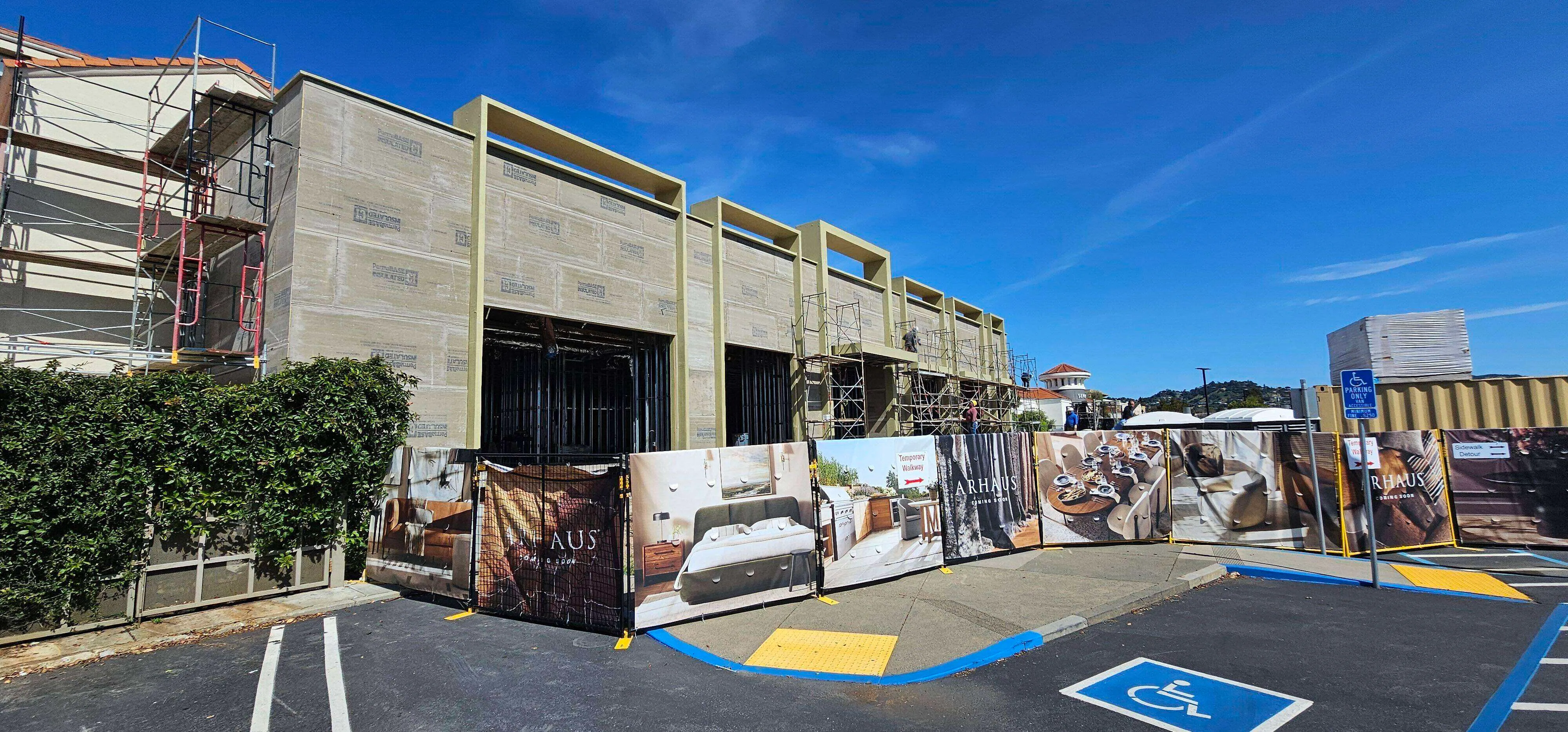 Commercial building under construction with scaffolding and advertisement banners in a parking lot.