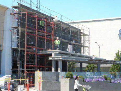 Scaffolding around a commercial building with workers, indicating ongoing construction or plaster work. — Larkspur area