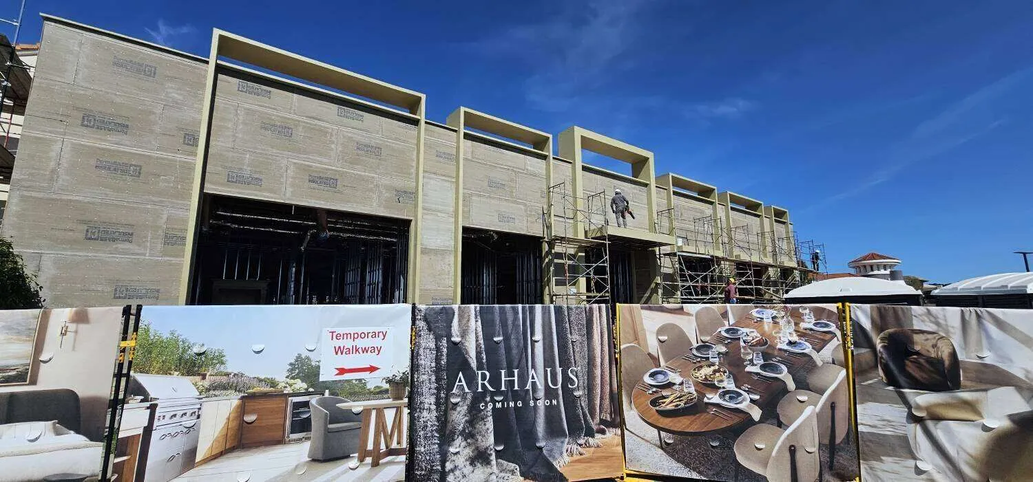 Commercial building under construction with scaffolding and temporary walkway signs.