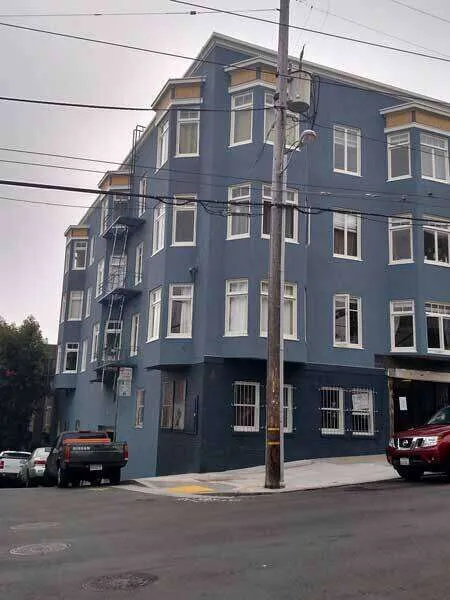 Multi-story blue stucco commercial building on a street corner with windows and fire escape.