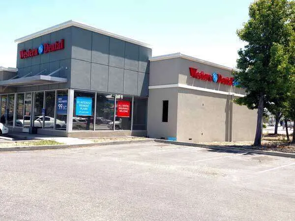 Modern commercial building with stucco exterior and large windows, housing a dental office.