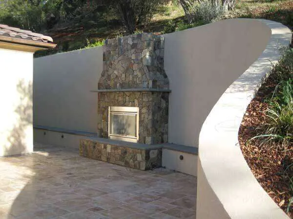 Curved concrete plaster wall with stone fireplace on a tiled outdoor patio.