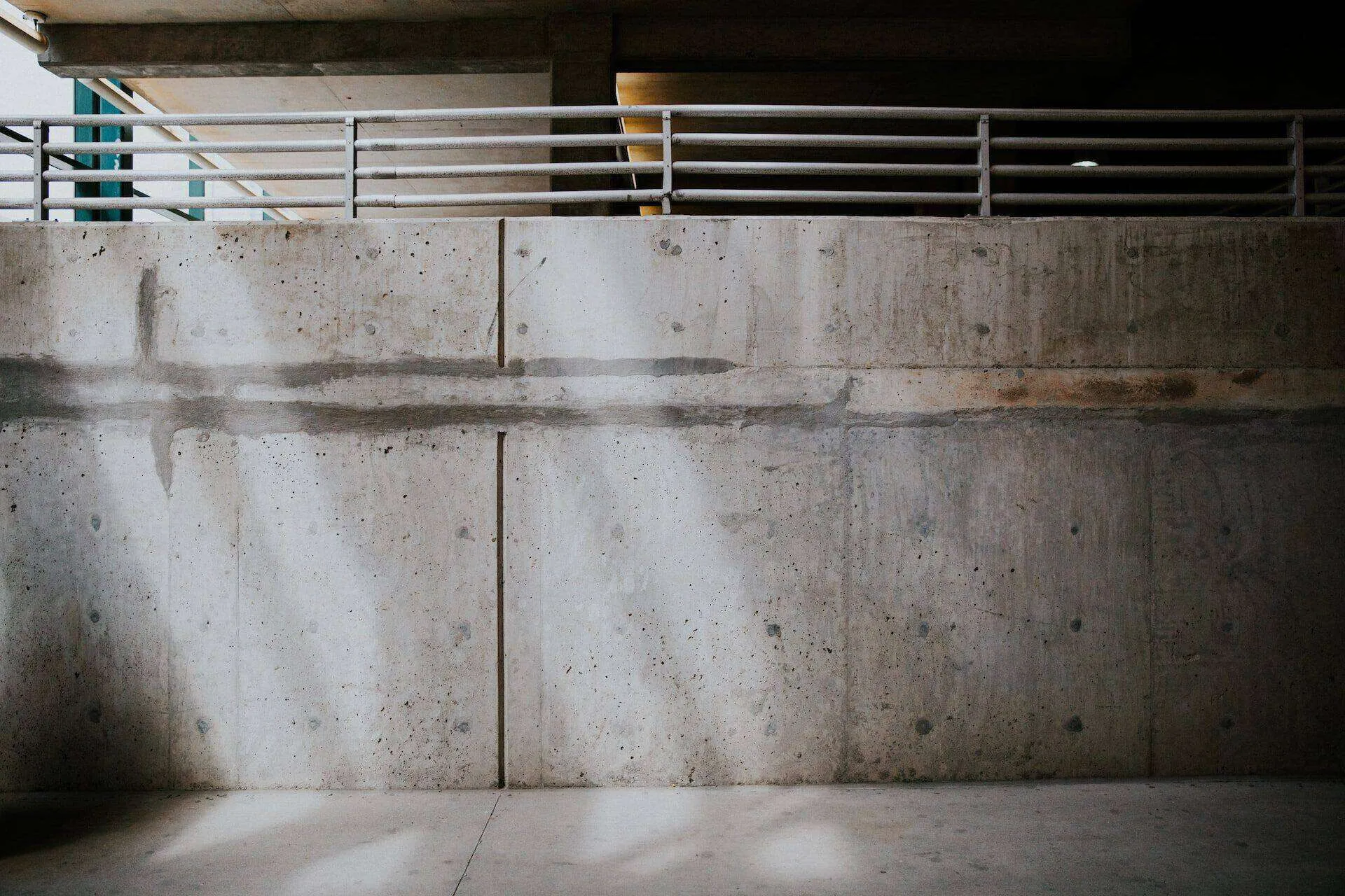 Concrete retaining wall with visible seams and metal railing in an outdoor urban setting.