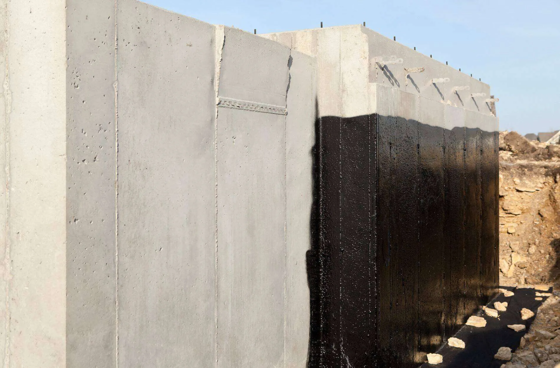 Concrete wall with black waterproofing membrane applied on one side, showing contrast with untreated concrete.