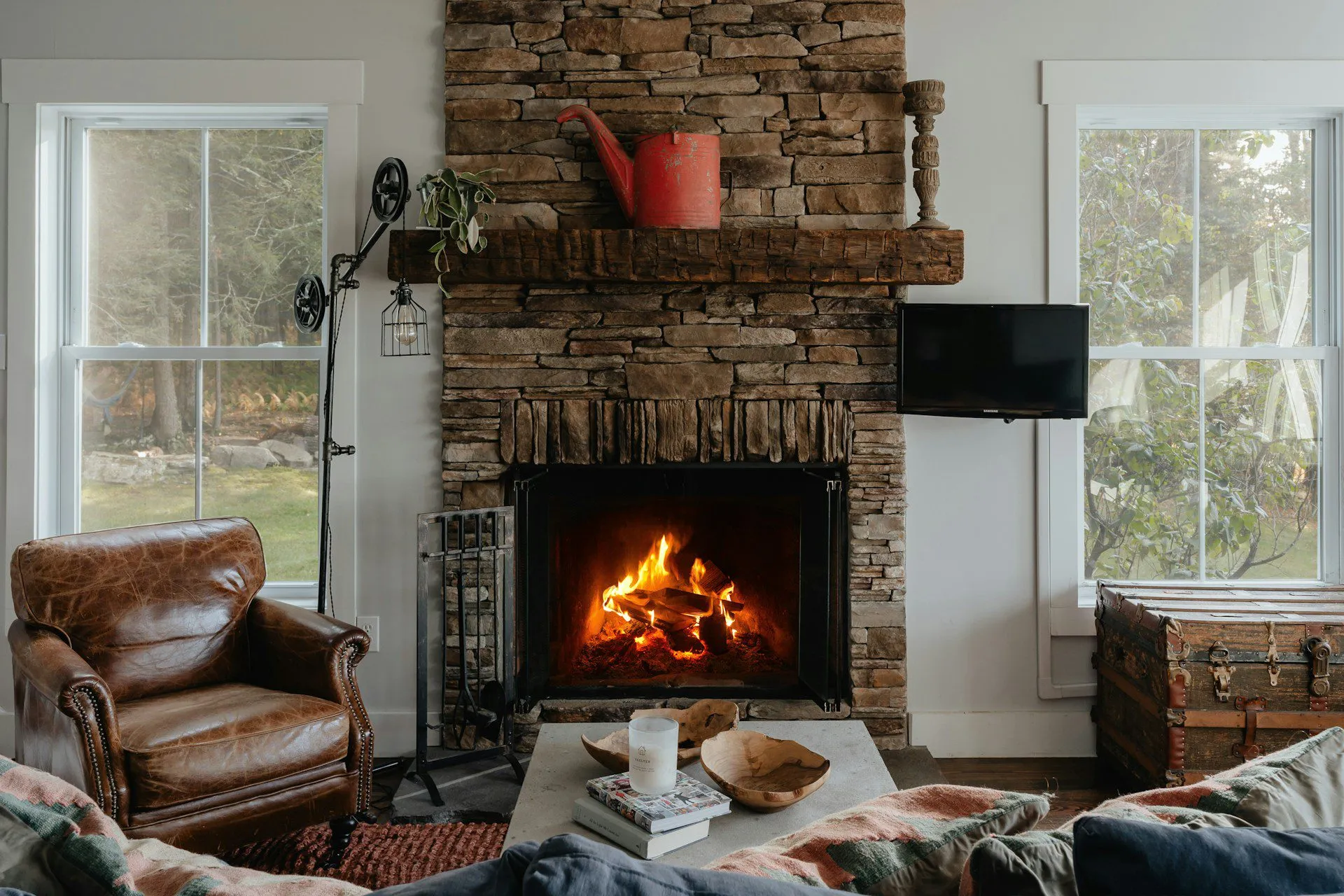 Living room with a stone fireplace, leather armchair, and windows on either side.