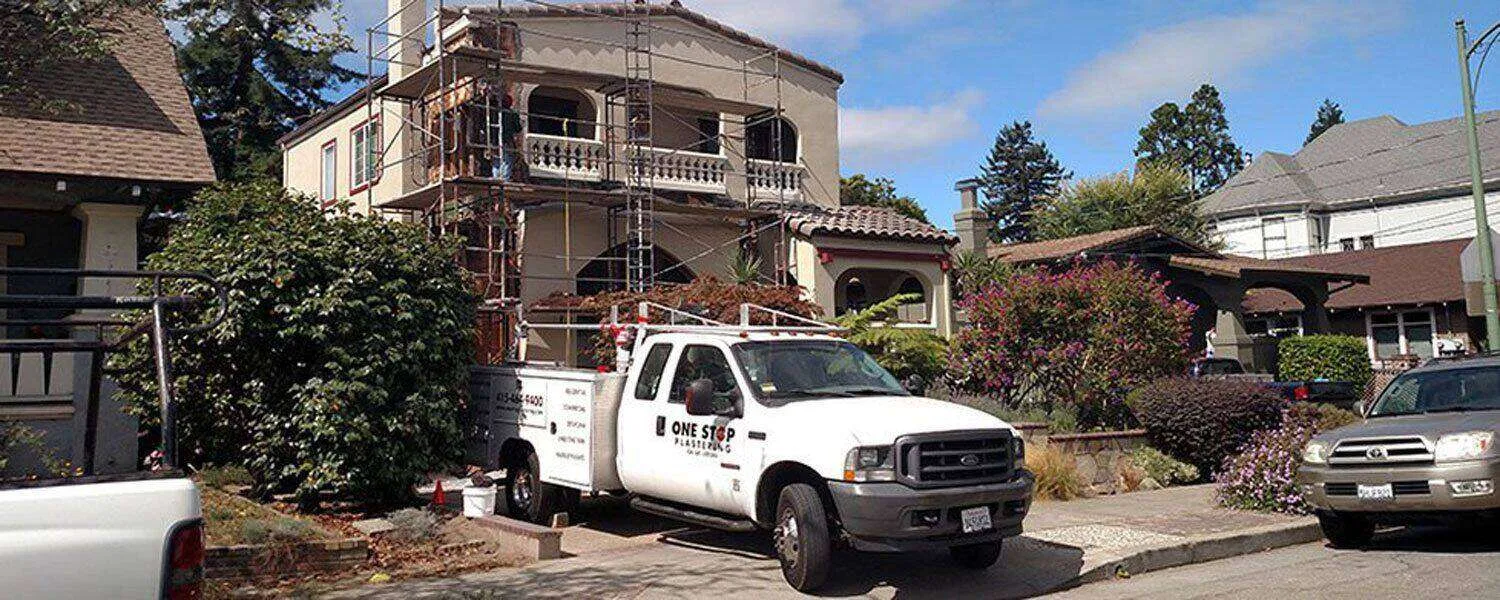 Residential building with scaffolding and One Stop Plastering truck indicating repair work.