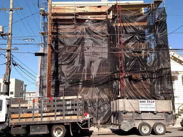 Building under construction with black tarps, scaffolding, and One Stop Plastering truck and trailer.