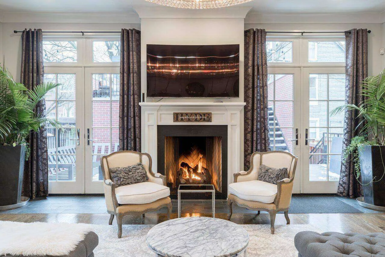 Living room with fireplace, TV, armchairs, and large windows with curtains.