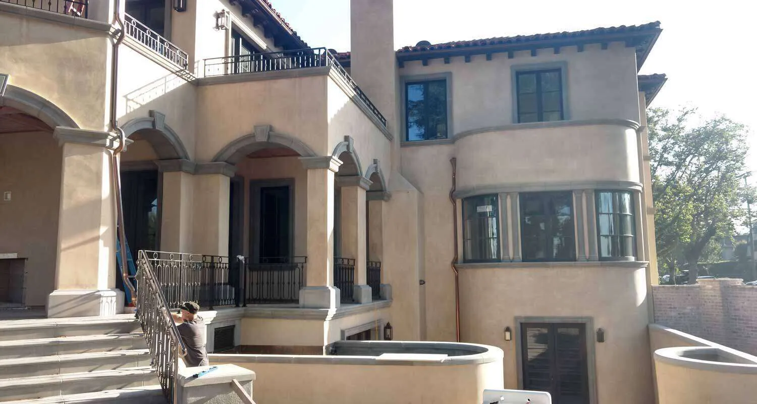 Large residential building with smooth stucco finish and arched details, person working on railing. — Richmond area