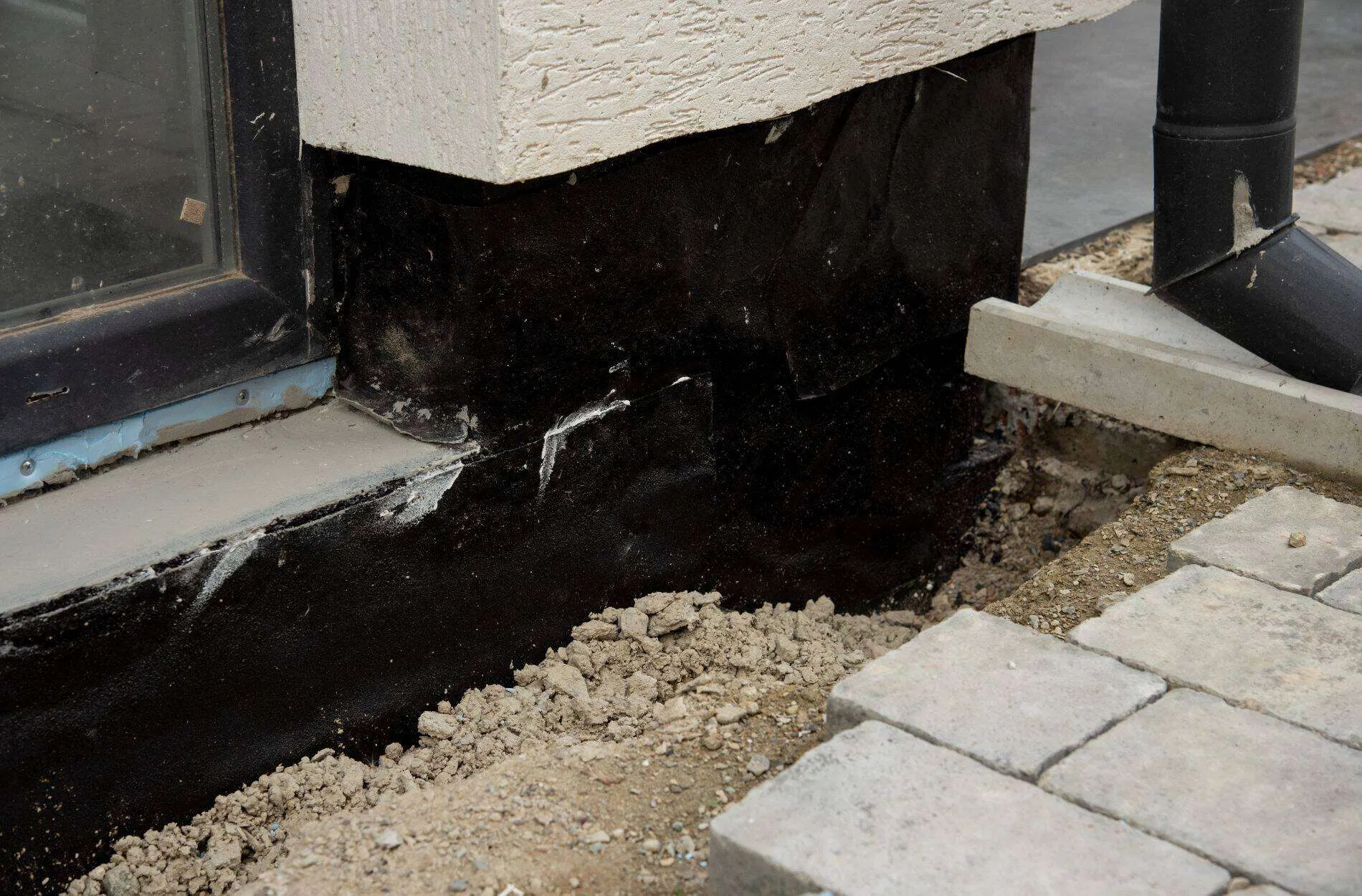 Close-up of a building foundation with waterproofing material applied, showing excavation and drainage setup.