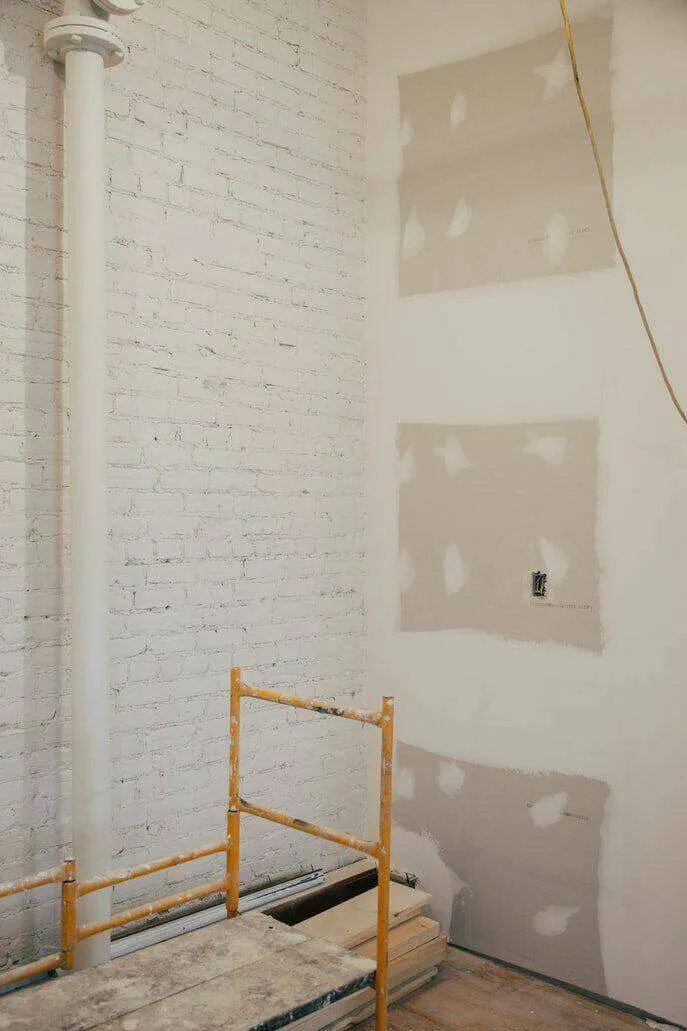 Interior construction site with drywall installation and a brick wall, featuring a scaffold.