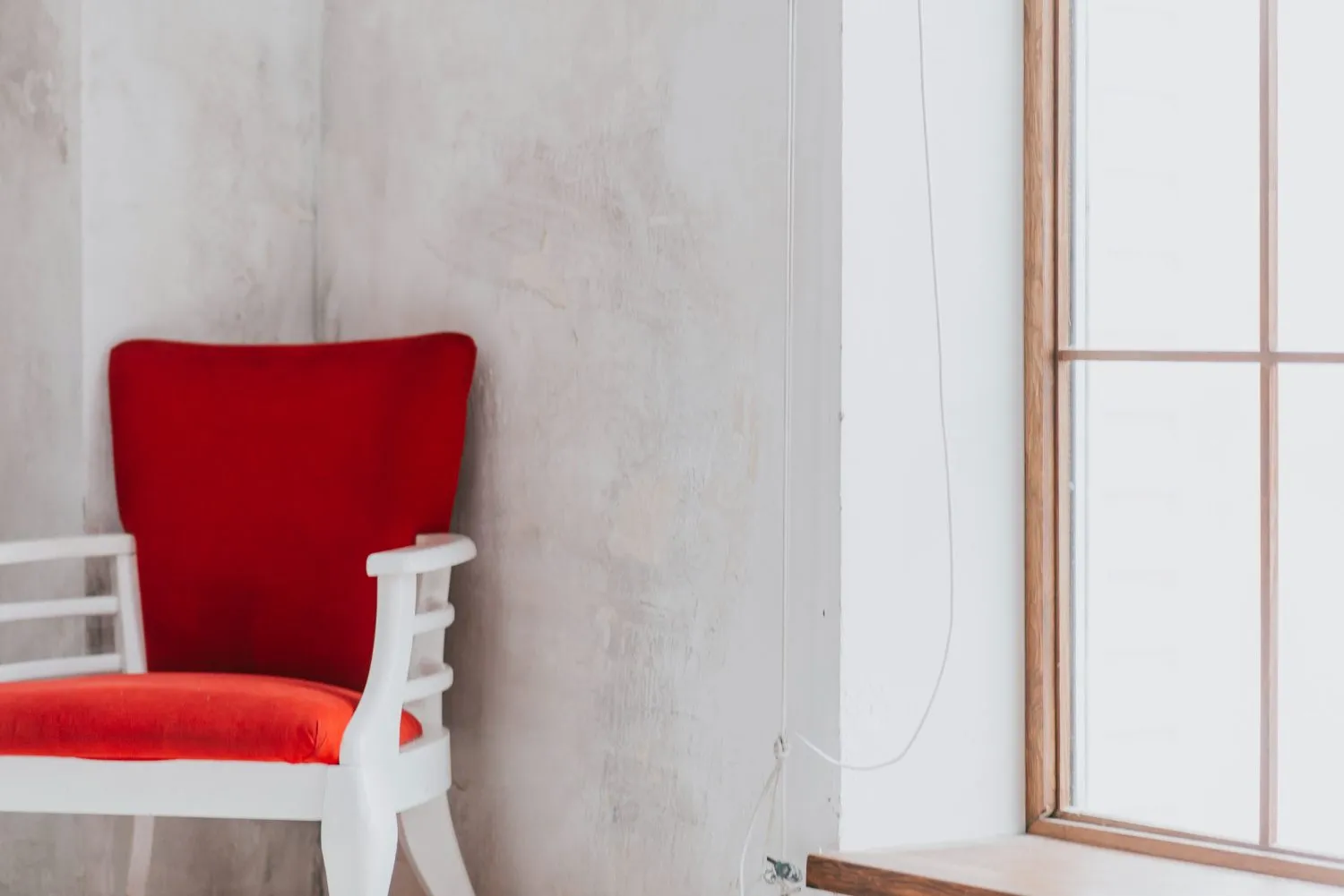 Corner of a room with a textured plaster wall, red-cushioned chair, and wooden-framed window.