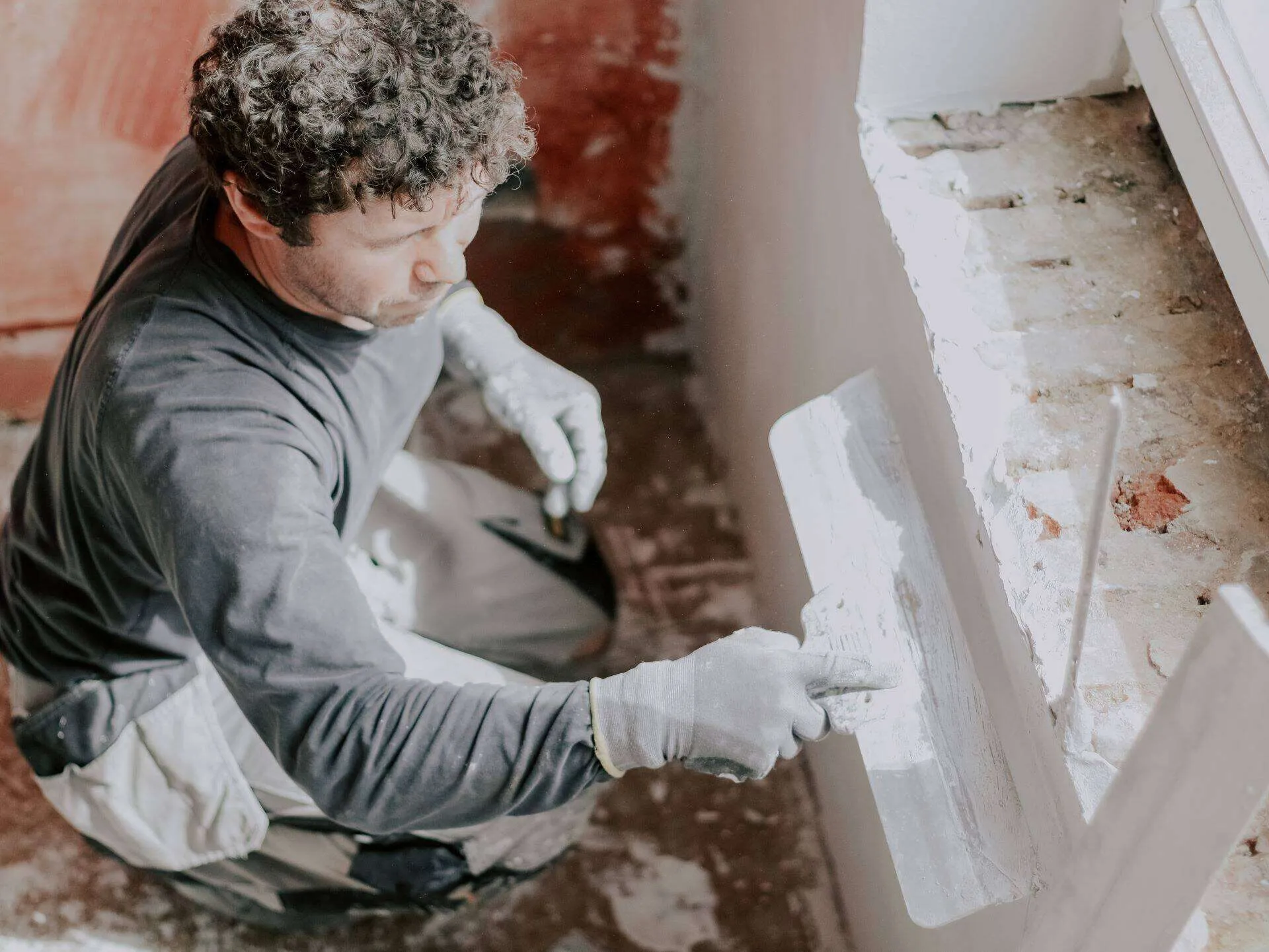 Person applying putty to a window frame with a trowel in an interior renovation setting.