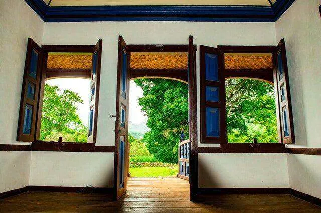 Room interior with wooden floors, open windows, and view of green landscape.