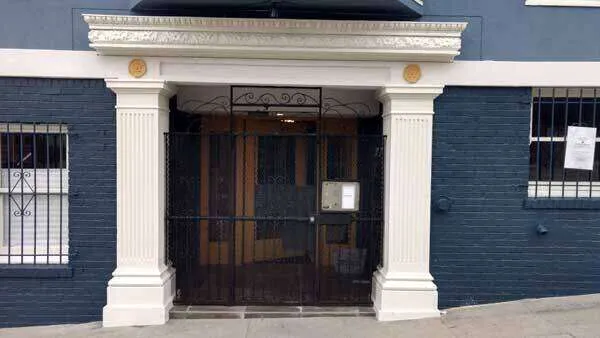 Building entrance with decorative foam trim columns and metal gate, dark blue facade.