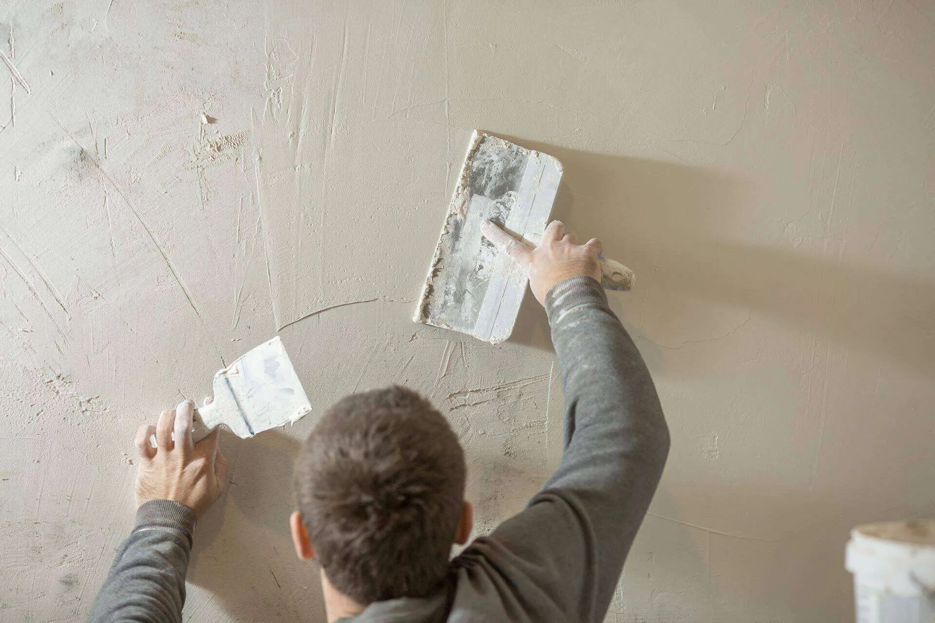 Man applying plaster to a rough wall with a spatula and trowel, showing repair work.