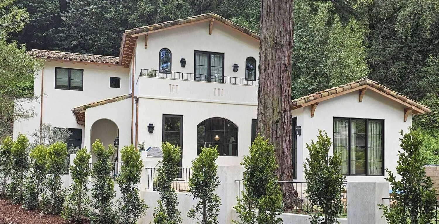 Mediterranean-style home with white stucco and terracotta roof in a wooded area.