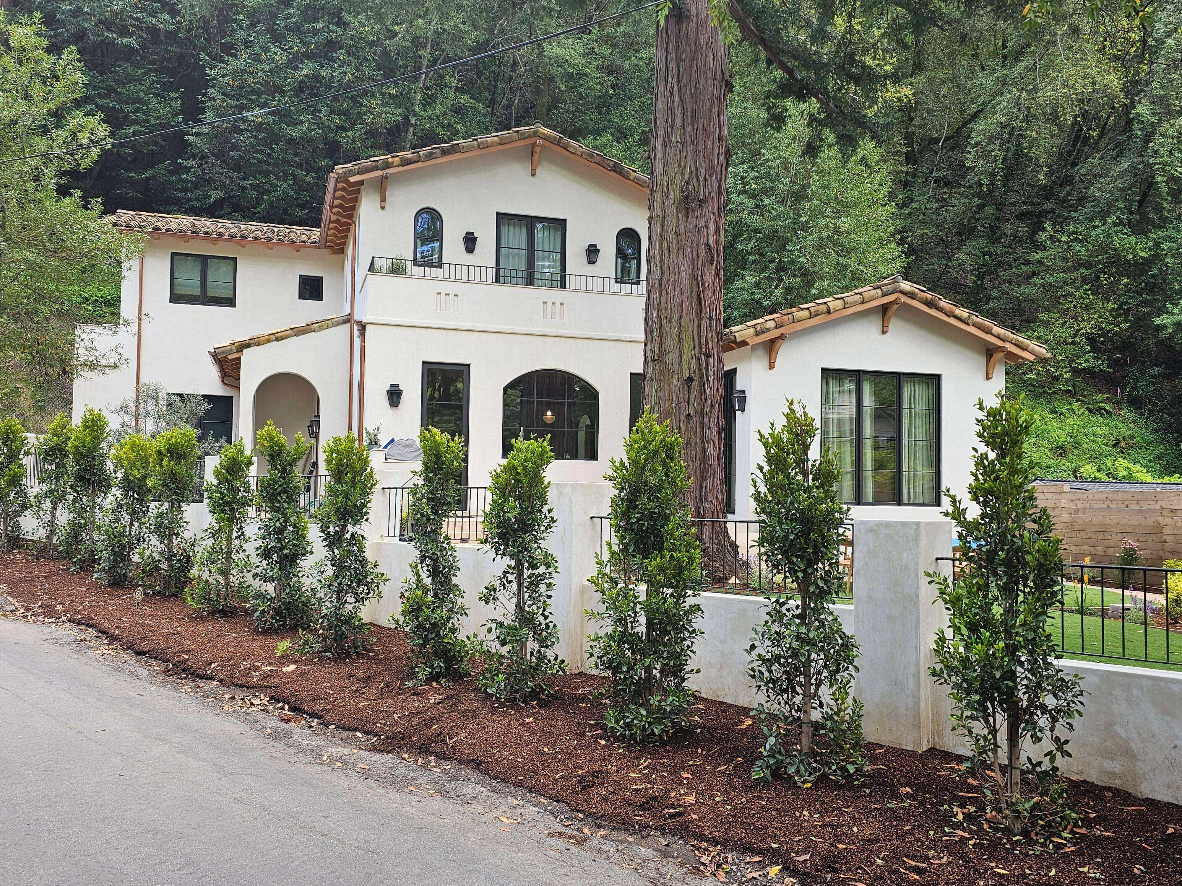 Mediterranean-style home with white stucco, tile roof, and landscaped yard in a wooded area. — Larkspur area