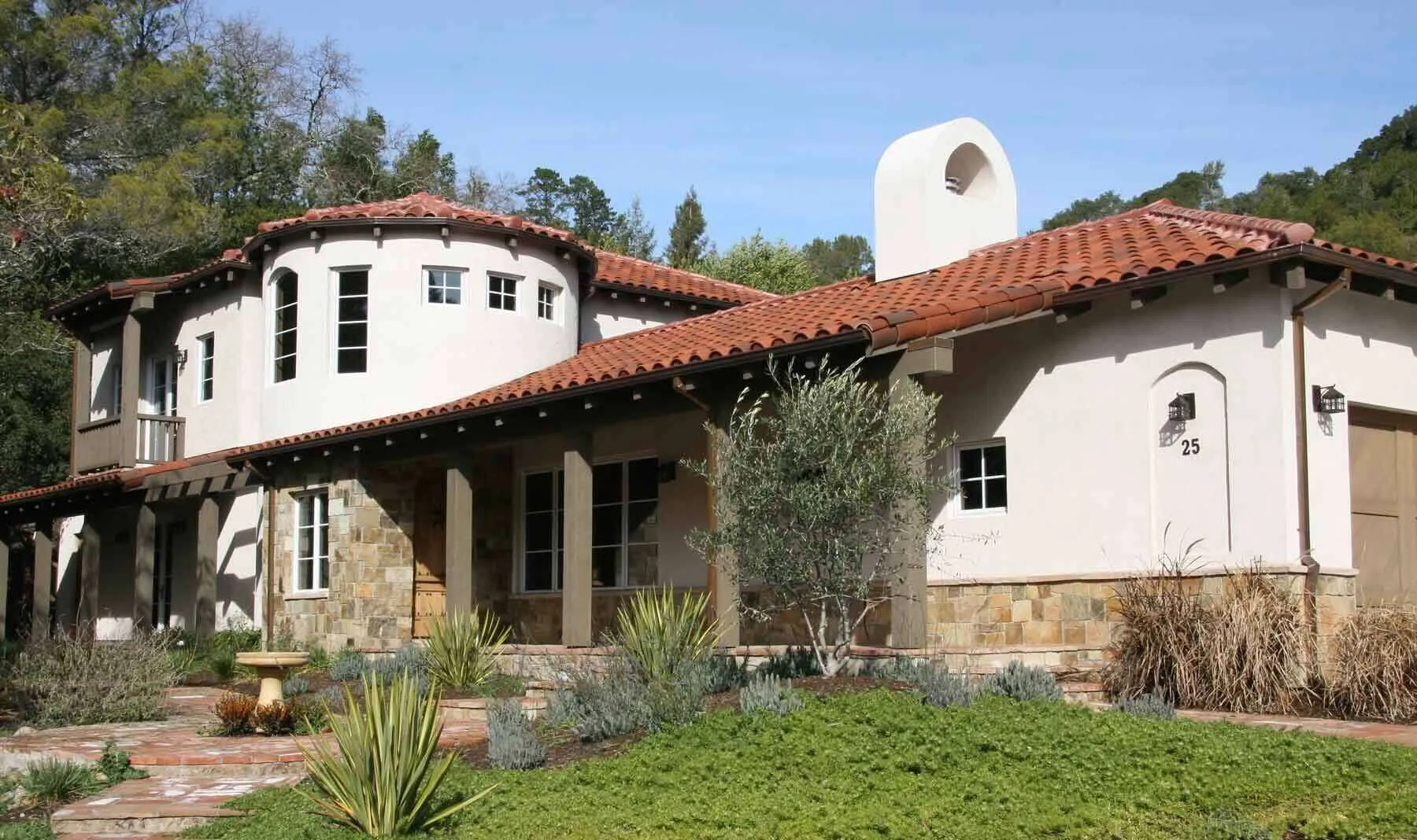 Mediterranean-style home with stucco walls, red tile roof, and arched windows in a lush setting. — San Anselmo area