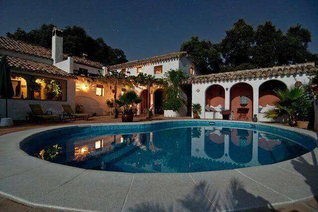 Night view of a Mediterranean-style stucco house with a pool and lit courtyard.