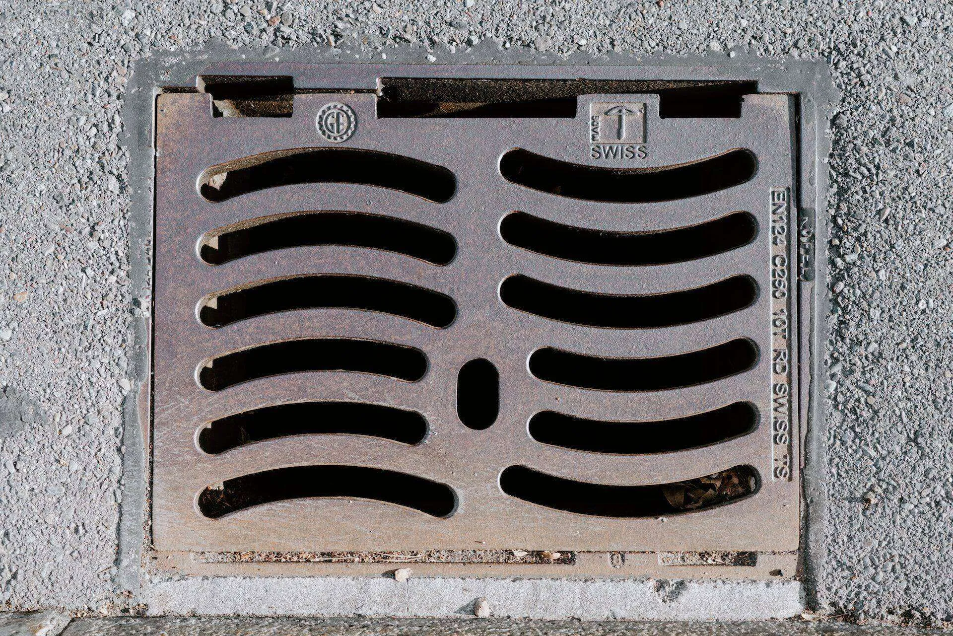 Metal drainage grate with curved slots embedded in a concrete surface for water management.