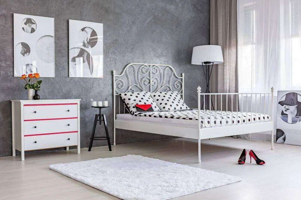 Bedroom with grey stucco wall, white metal bed, polka dot bedding, and abstract art on the wall.