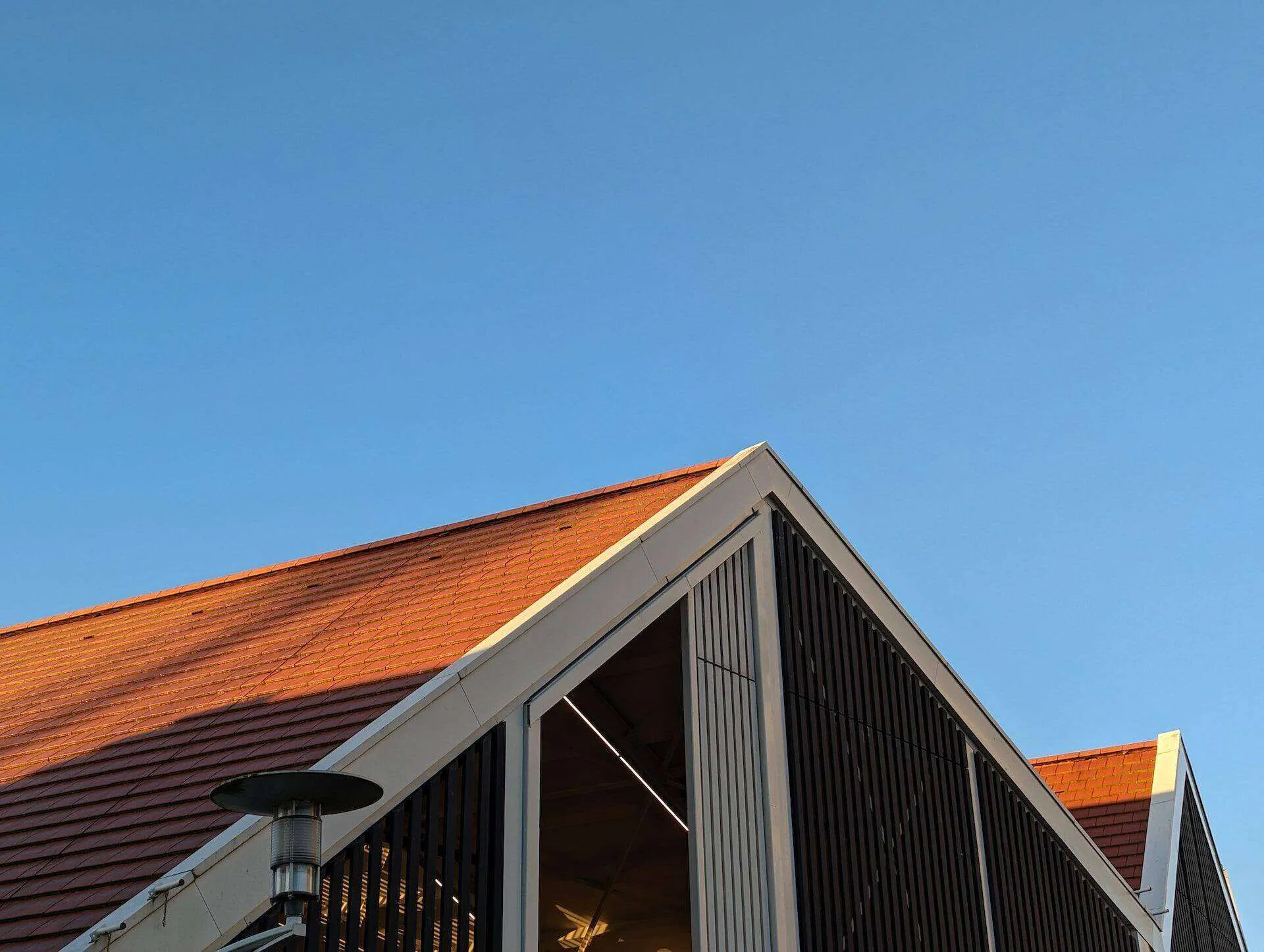 Modern building with red-tiled roof and vertical slatted siding against a blue sky.