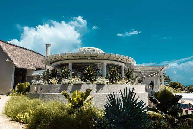 Modern circular building with landscaped retaining wall and plants under a clear blue sky.
