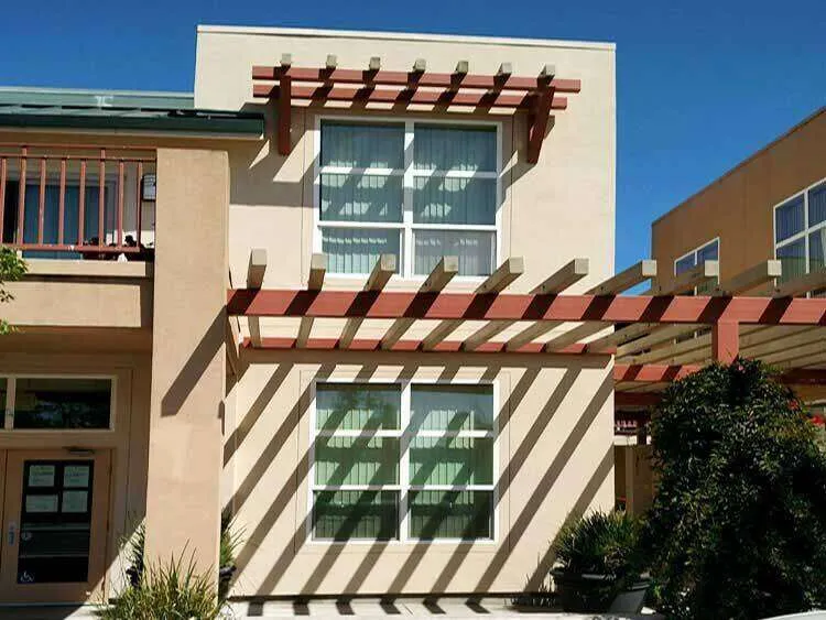 Modern building exterior with stucco finish and wooden pergola casting shadows. — Fairfax area