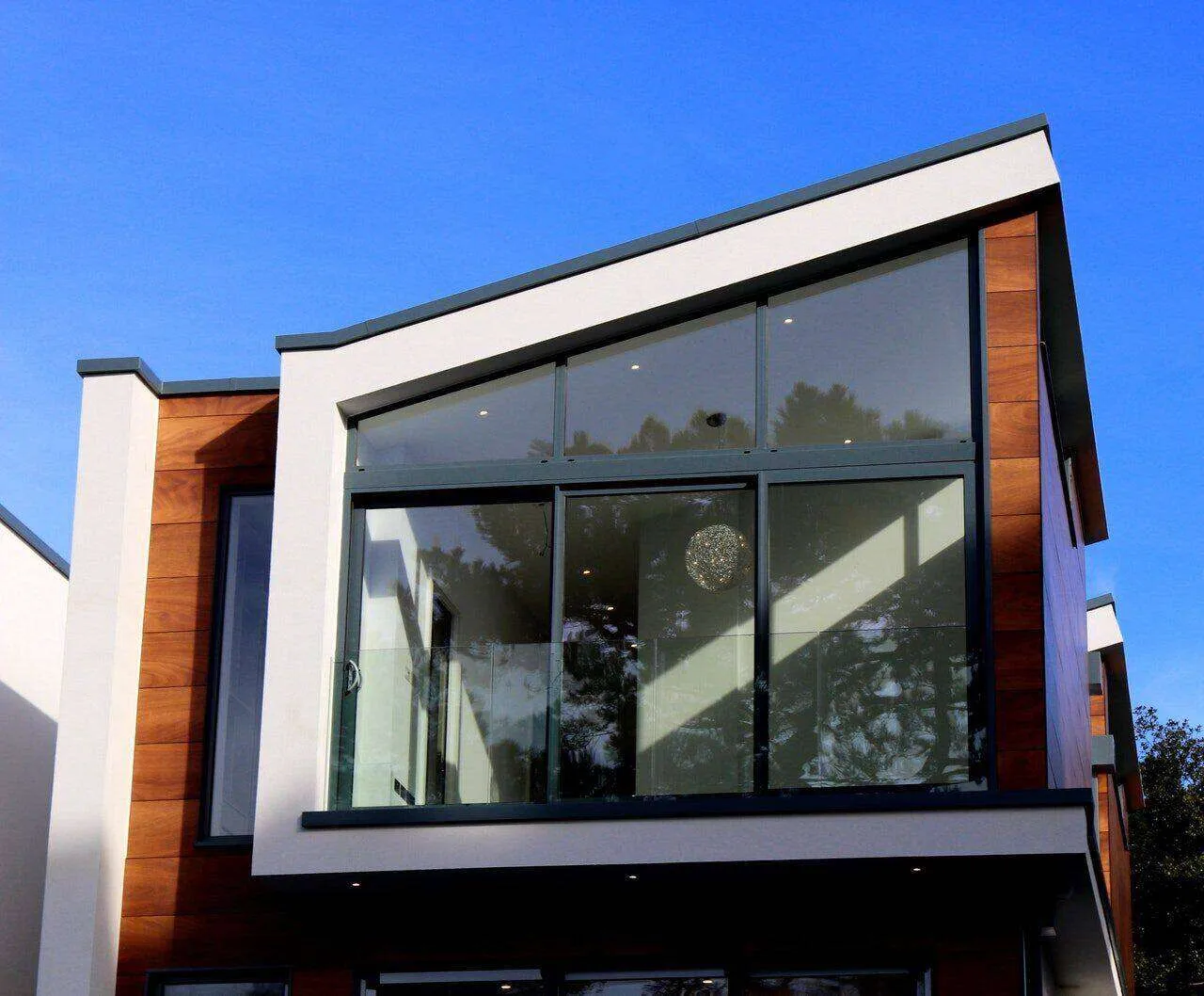 Modern house exterior with large glass windows and wooden paneling under a blue sky.