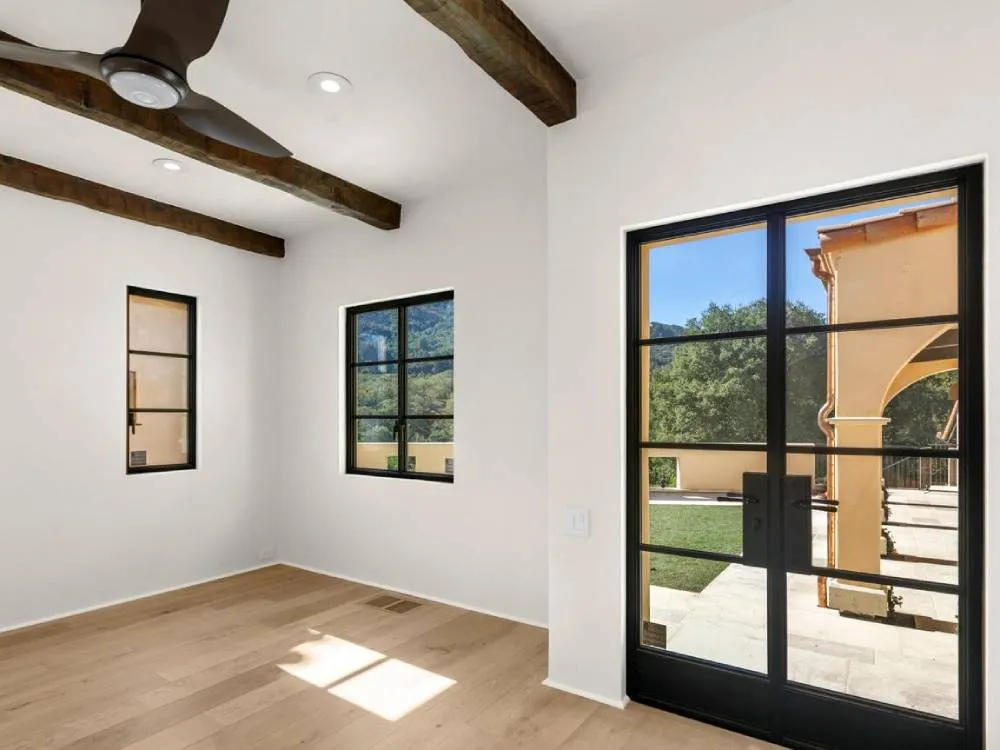 Interior room with wooden beams, light wood floor, and large black-framed windows and doors.