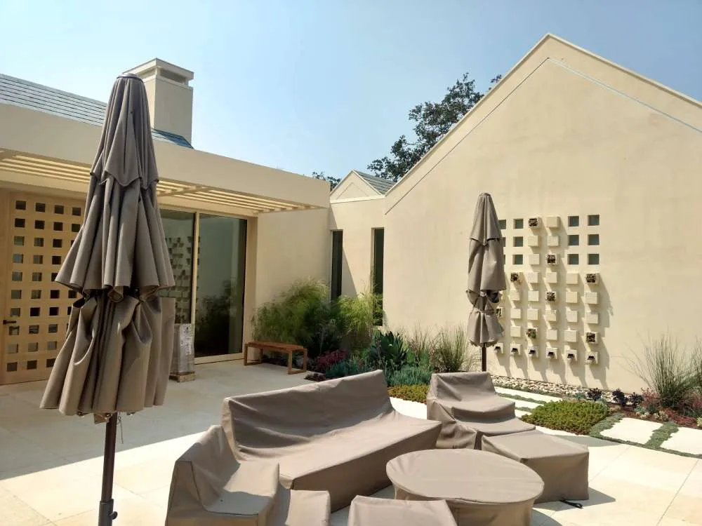Outdoor patio with beige stucco walls, covered furniture, and potted plants under a sunny sky. — Alameda area