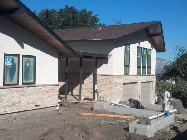 Modern residential home with stucco and stone veneer under construction, workers present. — El Cerrito area