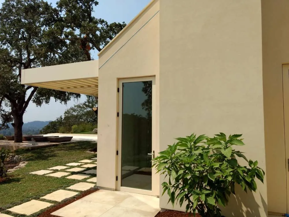Modern building exterior with smooth stucco finish, glass door, and landscaped area with stepping stones and plants. — Fairfax area