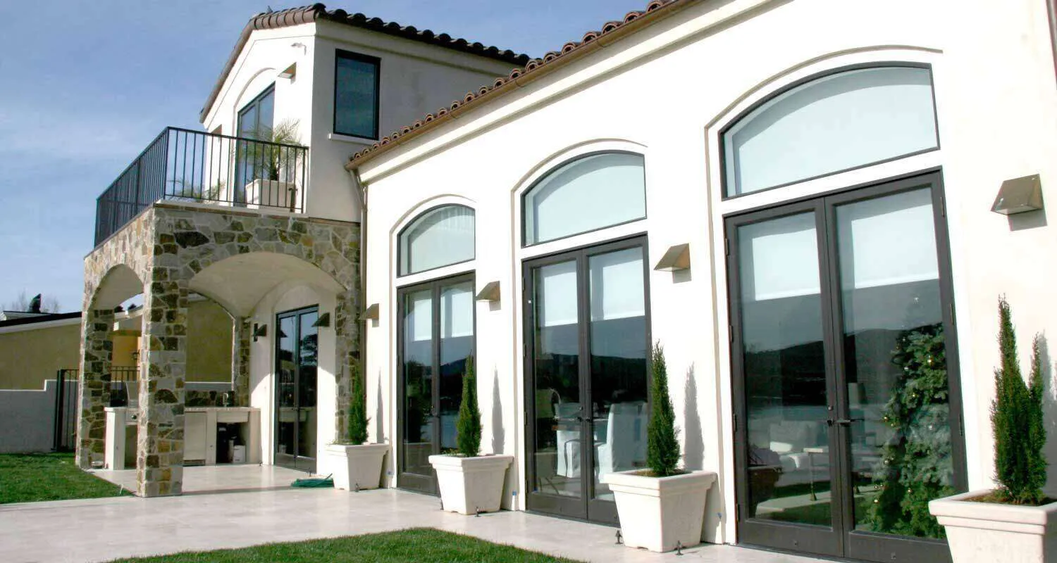 Modern house exterior with stucco finish, large windows, stone archway, and balcony.