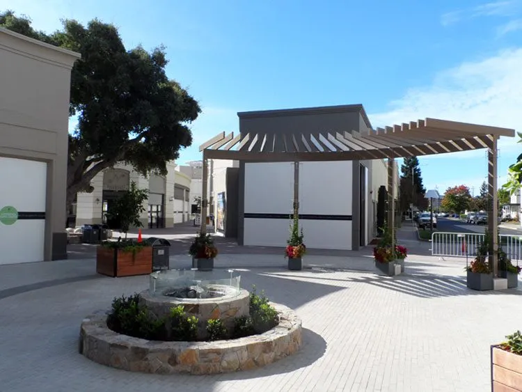 Commercial plaza with a pergola and stone fountain, EIFS finish on buildings.