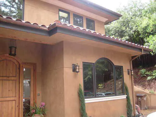 House exterior with smooth plaster finish, arched windows, and tiled roof. — work near Oakland