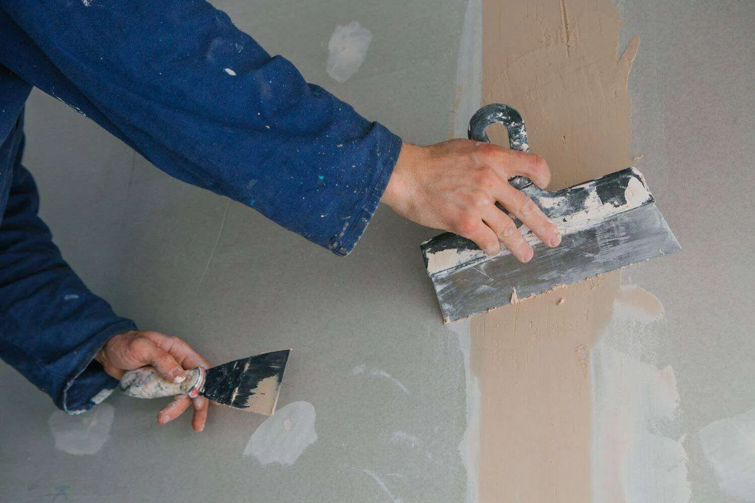 Person applying plaster to a wall with a trowel, smoothing the surface.