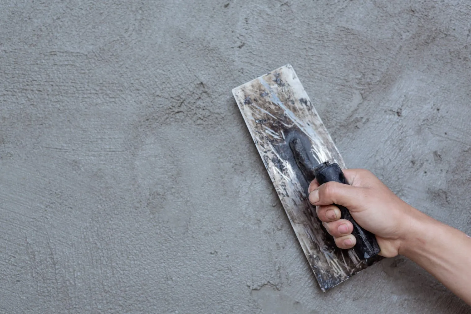Hand using a trowel to apply plaster on a wall, showing smooth texture.