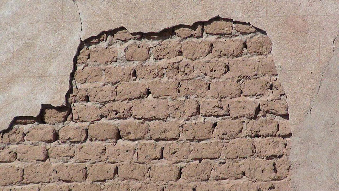 Wall with plaster damage exposing underlying bricks, showing cracks and missing plaster. — Larkspur area