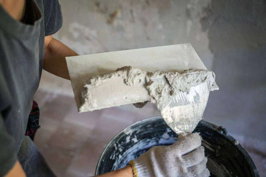 Close-up of a person applying plaster with a trowel onto a wall, showing the plastering process.